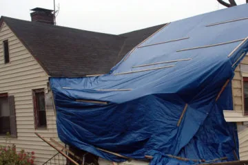 Storm-damaged residential roof covered with an emergency blue tarp — John Beal Roofing storm damage restoration in Branson, MO