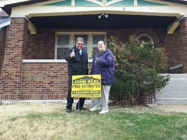 Homeowners with a John Beal yard sign outside their brick bungalow