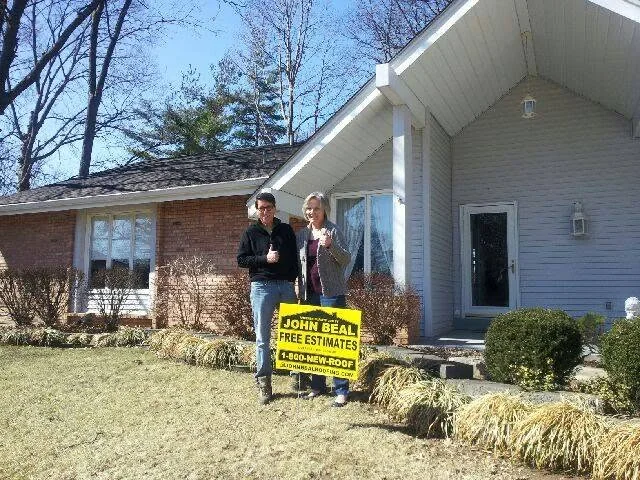 Couple giving a thumbs up in front of their brick ranch with a new roof