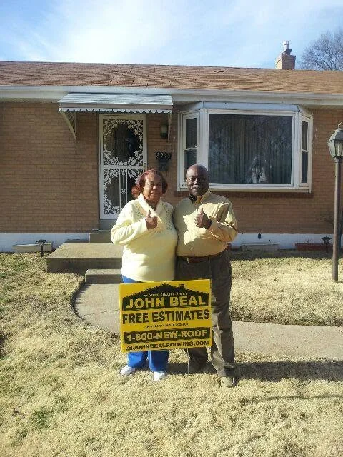 Homeowners giving a thumbs up beside a John Beal yard sign at their brick home