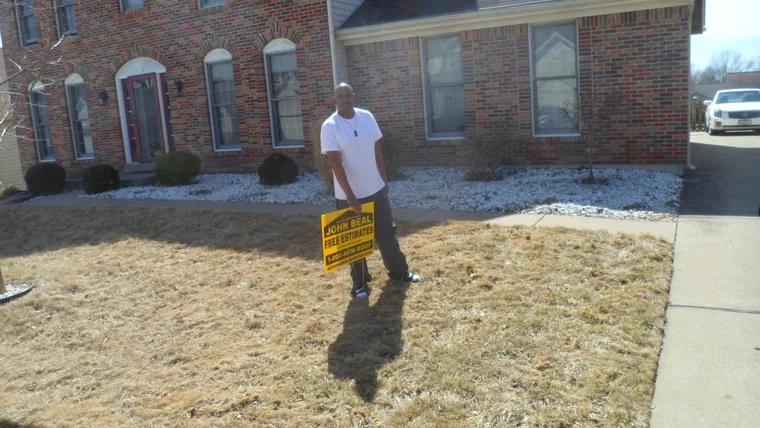 Homeowner holding a John Beal yard sign in front of a brick two-story home
