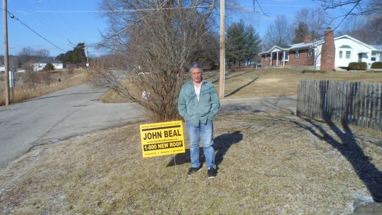 Homeowner beside a John Beal yard sign on a country lot