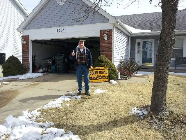 Homeowner with a John Beal yard sign outside his garage after a winter roof replacement