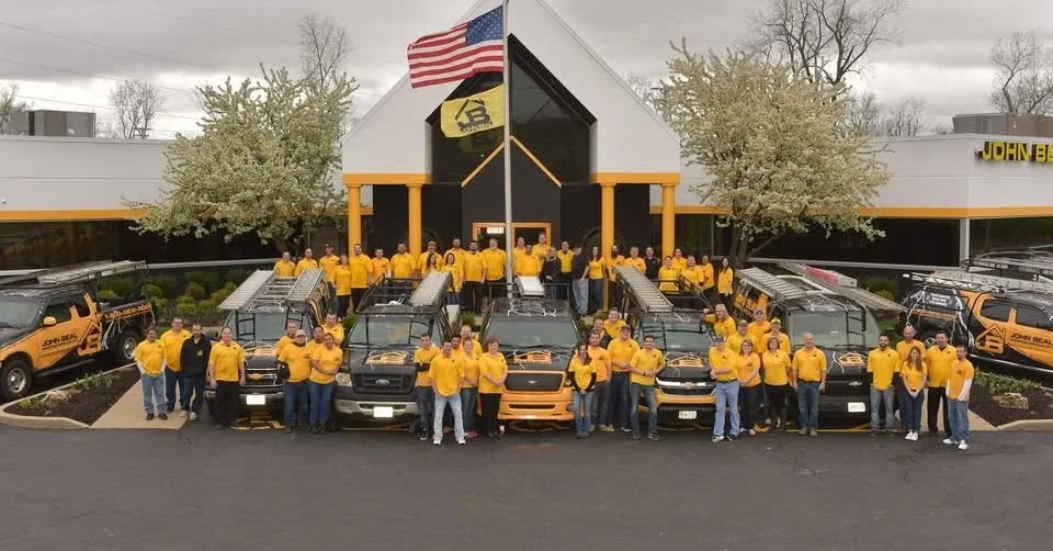 The John Beal Roofing team outside headquarters with the company truck fleet