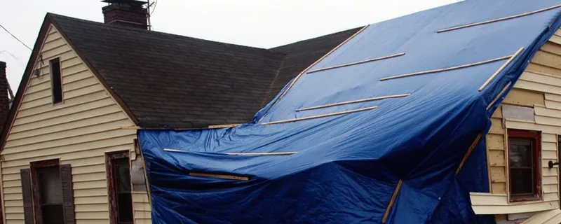 Home with severe roof damage covered by a blue emergency tarp — John Beal Roofing storm damage restoration in Branson, MO